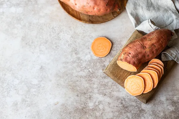 Ολόκληρες και φέτες ωμές γλυκοπατάτες σε ξύλινη σανίδα κουζίνας, βιολογική γλυκοπατάτα. Η γεωργική τροφή. — Φωτογραφία Αρχείου