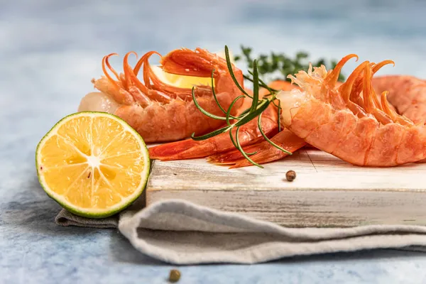 Camarões argentinos crus em tábua de corte de madeira branca com limão, ervas e pimenta. Frutos do mar. Fechar. — Fotografia de Stock