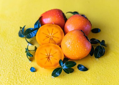 Sarı arka planda yapraklar ve su damlaları ile tüm ve yarım hurmaları kes.