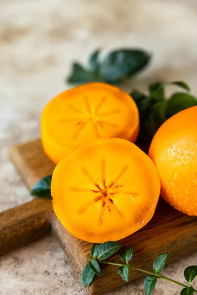 Whole and cut half ripe orange persimmon fruit on wooden cutting board, concrete background. — Stock Photo, Image