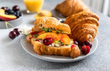 Nektarin, kiraz ve ricotta ile kruvasan sandviçi veya lezzetli kahvaltı için portakal suyuyla dolu bir tabakta krem peynir..