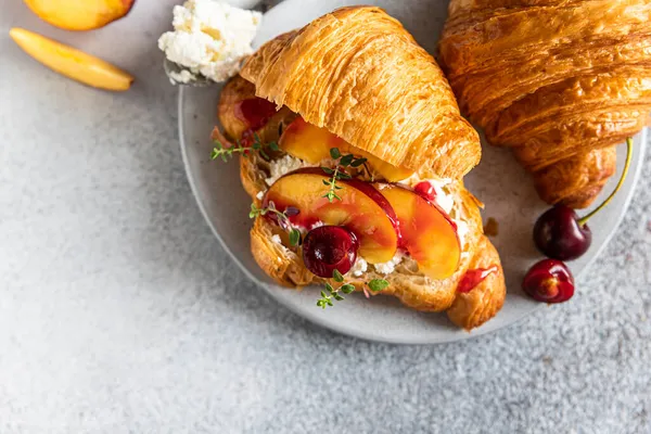 Croissant nektarinnal, cseresznyével és ricotta sajttal, szürke kő háttérrel. Finom reggeli. Felülnézet. — Stock Fotó