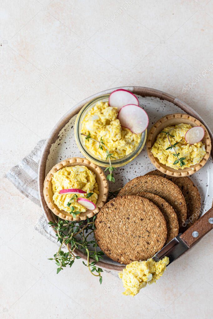 Plate with tartlets, multigrain crackers with egg pate or salad served with radish and thyme.