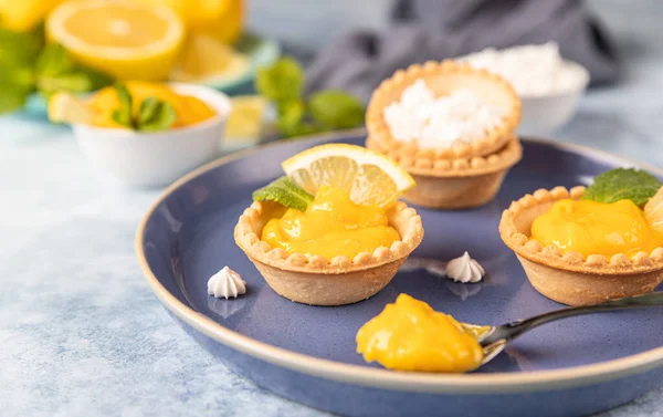 Mavi seramik tabakta naneli ve limon dilimli limonlu mini tartlar. Seçici odak.