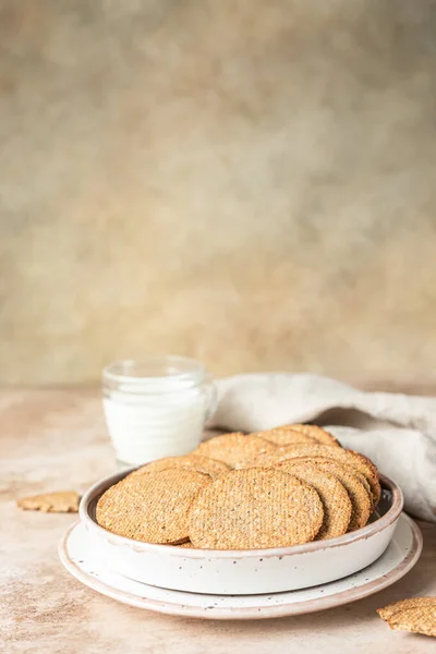 Tasty crackers with seeds on a plate and a cup of milk, brown background. Snack or breakfast. — Stock Photo, Image
