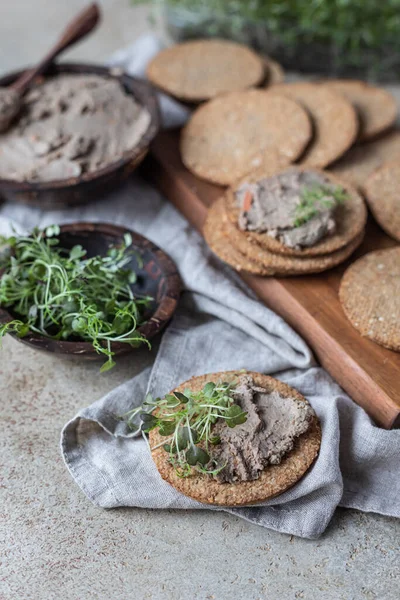 Домашнее мясо или куриный паштет с многозерновыми крекерами и микрозеленым, бетонным фоном. — стоковое фото