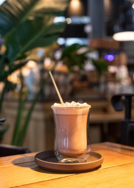 Sıcak çikolata ya da cam bardakta lokum kaplı kakao, ahşap masa, bulanık kafe arka planda. Tonu ayarlanmış resim.