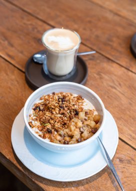 Breakfast with tasty oatmeal with caramelized apples and granola and glass of cappuccino on wooden table. Healthy food concept.