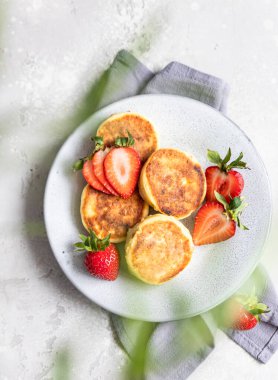 Cottage cheese pancakes or fritters with strawberry and natural yogurt on light background. Healthy breakfast or lunch. Syrniki. Top view.