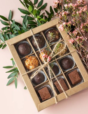 Hafif beton arka planda çeşitli çikolatalar ve pembe çiçeklerle bir hediye kutusu. Üst Manzara. Seçici odak.