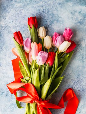 Bouquet of colorful tulips with red ribbon on blue concrete background. Beautiful tulips for Mother's Day or Easter. Selective focus.