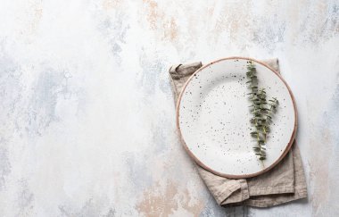 Boş beyaz tabak, keten peçete ve okaliptüs dalları, açık beton arka plan. Bahar menüsü kavramı. Moda minimal sofra takımı. Restoran için model menü. Üst görünüm, alanı kopyala.