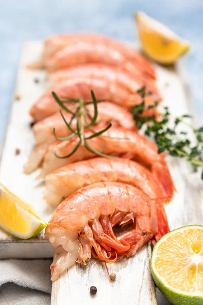 Camarões argentinos crus em tábua de corte de madeira branca com limão, ervas e pimenta. Frutos do mar. — Fotografia de Stock