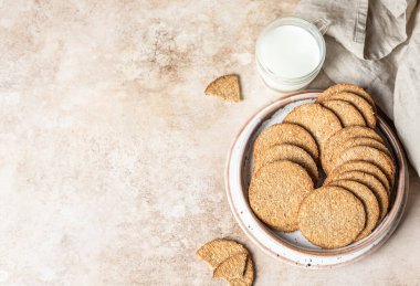 Lezzetli krakerler, tabakta tohum ve bir fincan süt, kahverengi arka plan. Atıştırmalık ya da kahvaltı. Üst görünüm.