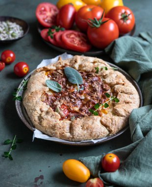 Baharatlı domates turtası, açık turta veya domatesli galet ve yeşil arka planda aromatik otlarla süslenmiş peynir..
