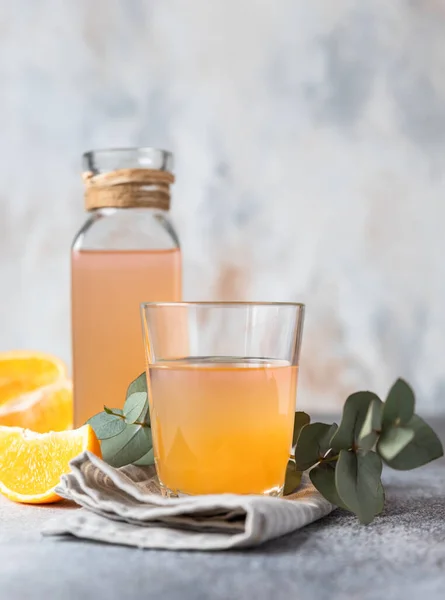 Kalter und erfrischender frischer Orangensaft in Glas und Flasche mit frischem orange-grauem Hintergrund. — Stockfoto
