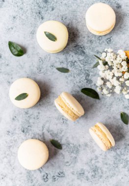 Fransız badem kurabiyelerinin pastel renkleri ve gri beton arka planda çingene çiçekleri. Üst görünüm.