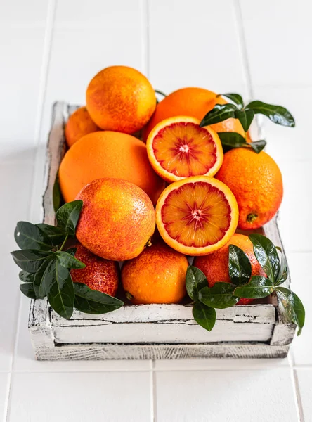 Ripe red Sicilian oranges with leaves in white wooden tray on white tiled background. Blood oranges.