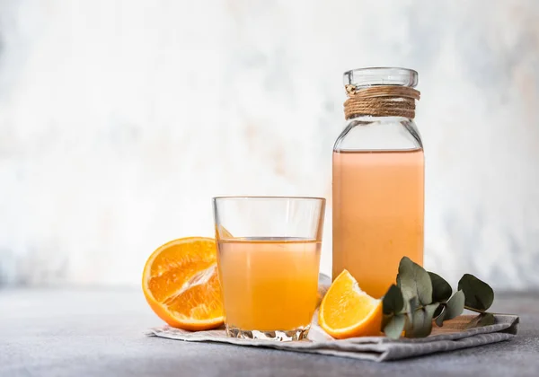 Orangenlimonade in Glas und Flasche mit frischem orangefarbenem Betonhintergrund. Erfrischendes Sommergetränk. Hintergrundkonzept Cocktailbar. — Stockfoto