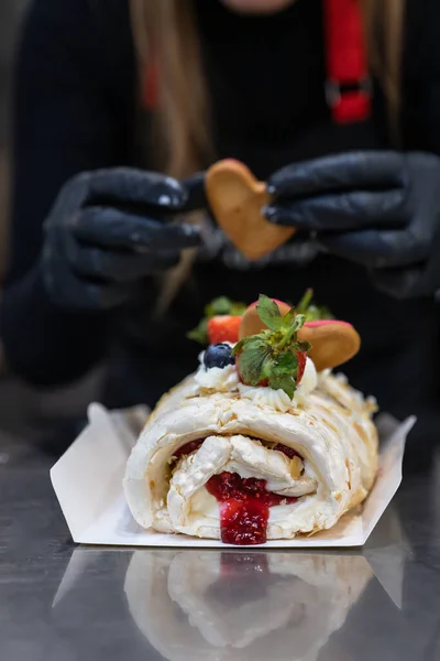 The process of making a meringue roll. The pastry chef decorates meringue cake with cream, berries and cookies. Confectionery