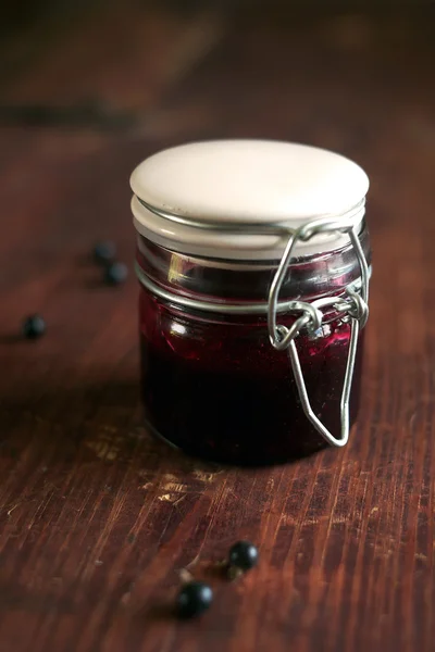 Fresh homemade blackcurrant jam, confiture or marmalade in a glass jar with blackcurrant berries on the wooden table, rustic style, selective focus