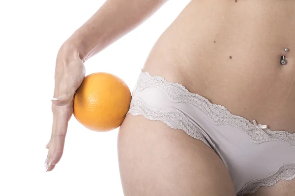 Attraktiv ung kvinna håller en orange till hennes lår — Stockfoto