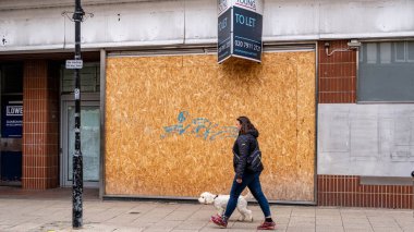Kingston Londra 'da İngiltere 5 Kasım 2021' de kapanmış perakende mağazasının arka planda kalmasına izin vermek için köpeğini gezdiren kadın.