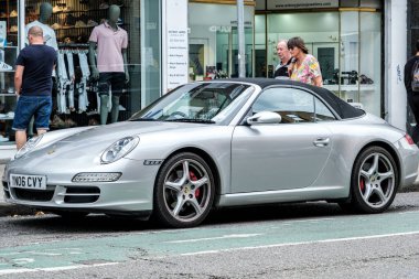 Kingston-Upon-Thames, London, UK, August 29 2022, Convertable Silver Porsche 911 Parked On A Main Street With Shoppers Browsing In Shop Windows