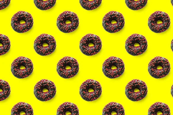 Black donuts with red glaze on yellow background seamless pattern top view. Food dessert flatly flat lay of delicious sweet nibbles chocolate donuts.