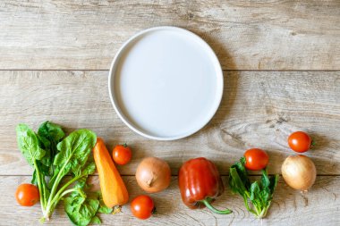 Organik ve bio taze sebzeler sıra sıra dizilmiş ve ahşap kırsal masa arka planında boş seramik tabağı var. Sağlıklı doğal olgun sebze konsepti. Salata, tarım ürünleri mağazası malzemeleri.