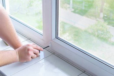 Erkek işçi elleri paten panjurlarına, perdelere, plastik pencere ekranlarına tornavidayla monte etme desteğini yerleştiriyor. Kopyalama alanı ile kapatın.