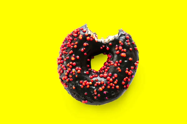 Creative concept of biting eating delicious sweet sugar black donghnut donut with red glaze bited on yellow background. Концепция нездорового десерта — стоковое фото