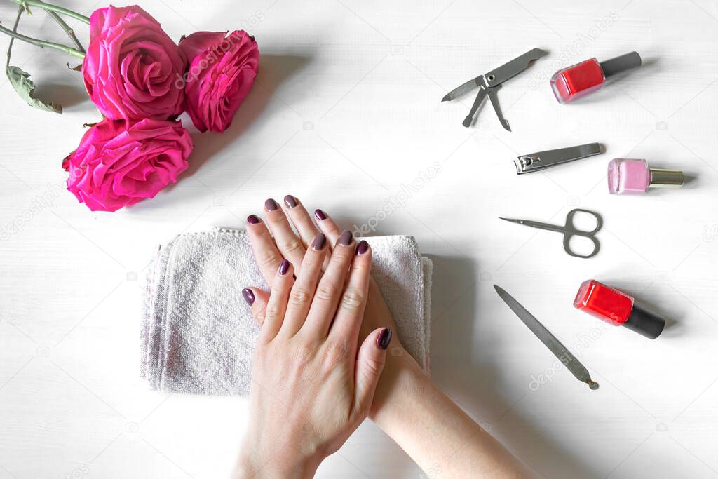 Closeup of woman hands with polished nails and manicure instruments, bottles of nail polish. receiving french manicure at home or at nail salon. selfcare, beauty procedures yourself.
