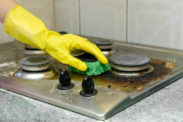 Cleaning dirty gas stove from grease, food leftovers deposits. womans hand in protective glove with sponge rag and detergent washing kitchen stove. home cleaning service concept