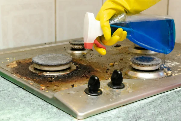 Kirli gaz sobasını yağdan temizlemek, yemek artıkları. Kadınlar koruyucu eldiveni sünger bezi ve deterjanı şişeye koyup mutfak sobasını yıkıyorlar. ev temizliği hizmeti kavramı — Stok fotoğraf