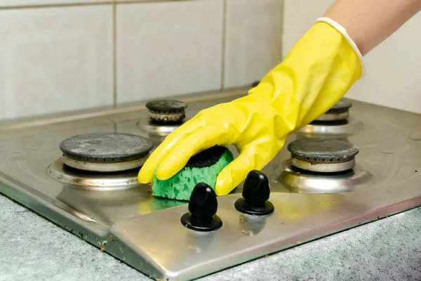 Cleaning dirty gas stove from grease, food leftovers deposits. woman\'s hand in protective glove with sponge rag and detergent washing kitchen stove. home cleaning service concept.