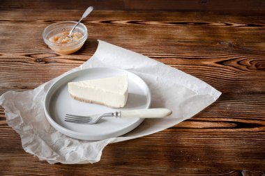 Lezzetli tatlı klasik cheesecake New York dilimi ahşap kırsal arka planda. Tatlı çatalı ve elma reçeli ile servis edilen seramik tabakta bir dilim lezzetli kek.