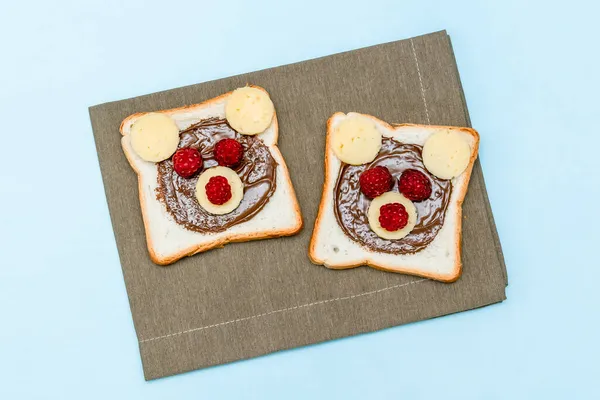 Drôle d'ours visage pain grillé sandwich avec beurre d'arachide, fromage et framboise sur fond bleu serviette. Enfants enfant dessert sucré déjeuner nourriture déjeuner fermer — Photo