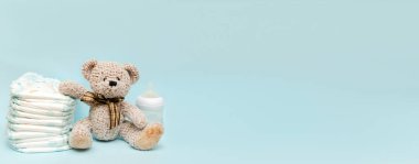 Oyuncak ayıyla bebek bezi yığını, masada bir şişe süt. Bebek partisi için hazırlandı. Mavi arka plan, afiş, fotokopi alanı. Sağlık sigortası, hijyen konsepti