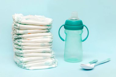 Bir yığın bebek bezi, şişe sütü, emzik, masada kaşıklar. Bebek için hazırlanmış yeni doğmuş kız bebek hediyesi olarak mavi arka planda. Sağlık sigortası, hijyen konsepti