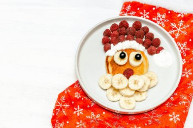 Noel Baba, tatlı taze ahududu ve muzlu krep şeklinde tabakta kırmızı çorap beyaz tahta arka planda çocuklar için kahvaltı. Yeni yıl süslemeleri ile xmas yemekleri
