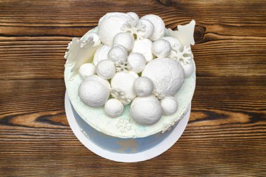 Beyaz mavi hindistan cevizi lezzetli vanilyalı kremalı pasta büyük yuvarlak marşmelov, çikolata kar taneleri, köknar ağaçları, ahşap masa manzaralı tatlı tatlı