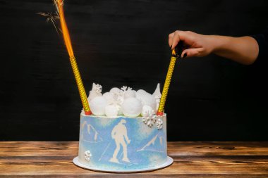 Havai fişek yakan kadın el feneri, mavi sünger vanilyalı pasta, yuvarlak marşmelov, çikolatalı kar taneleri, köknar ağaçları, dağ, kayakçı resmi, ahşap masadaki tatlı.