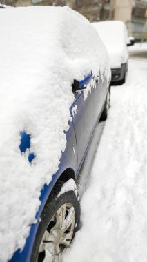Ön camda kar tabakası, şehir yolundaki otoparkın penceresinde sedan var. Kışın şiddetli kar fırtınasından sonra araba sıkıştı. Şiddetli hava koşullarında kar yağışı ve araç.