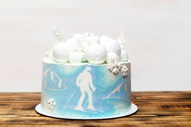 Beyaz mavi hindistan cevizi lezzetli vanilyalı kremalı pasta büyük yuvarlak marşmelov, çikolata kar taneleri, köknar ağaçları, dağ ve kayak resmi, ahşap masadaki tatlı tatlı tatlı tatlı.