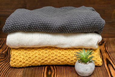 Kışlık kıyafetlerle dolu bir gardırop. Bir yığın katlanmış kaşmir sıcak yün örgü süveter. Sonbahar, kış soğuk sezonu örgü örer ahşap masada.