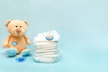 Masada oyuncak oyuncak bebek bezi yığını var. Bebek için hazırlanmış yeni doğmuş kız bebek hediyesi olarak mavi arka planda. Sağlık sigortası, hijyen konsepti.