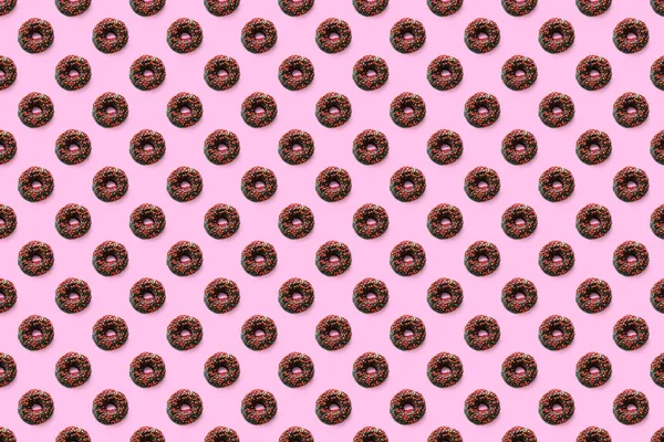 Black doughnuts with red glaze on pink seamless pattern background top view. Food sugar dessert flatly flat lay of delicious sweet nibbles chocolate donuts.