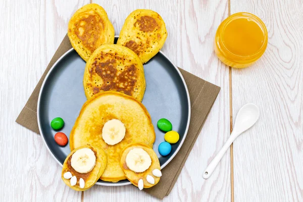 Paskah lucu kreatif sarapan makan siang yang sehat ide untuk anak-anak, anakren.Bunny, kelinci yang terbuat dari pancake, pisang dengan madu, permen manis, telur di piring meja background.Top tampilan Flat berbaring — Stok Foto