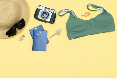 Seyahat tatili düz yatak, aksesuar nesneler, şapka, pasaport, güneş gözlüğü, kıyafet, mayo, kamera, deniz kabuğu fotokopi alanı olan sarı arka plan, planlama macerası.